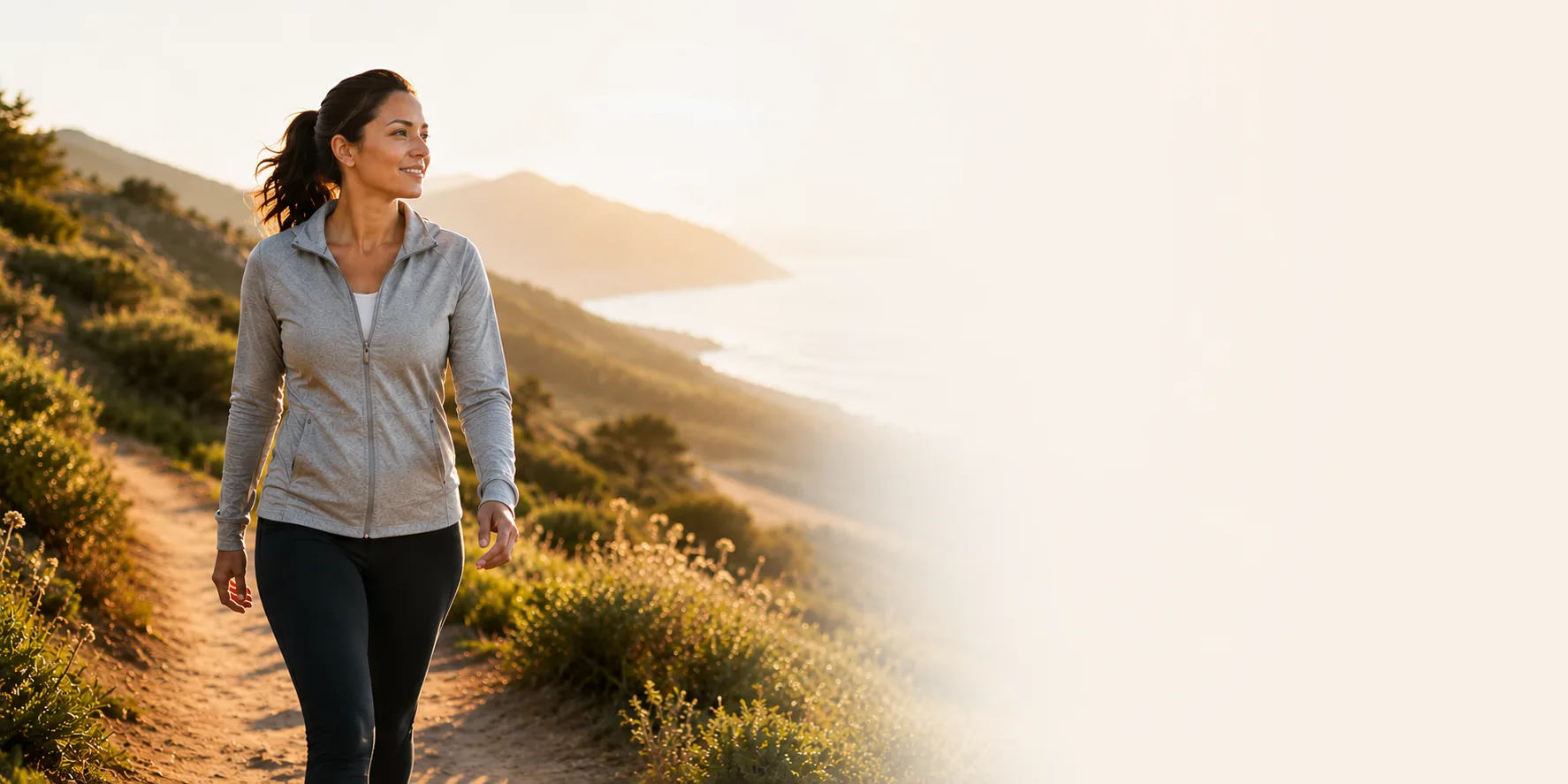 A smiling woman walking on a coastal trail at sunrise